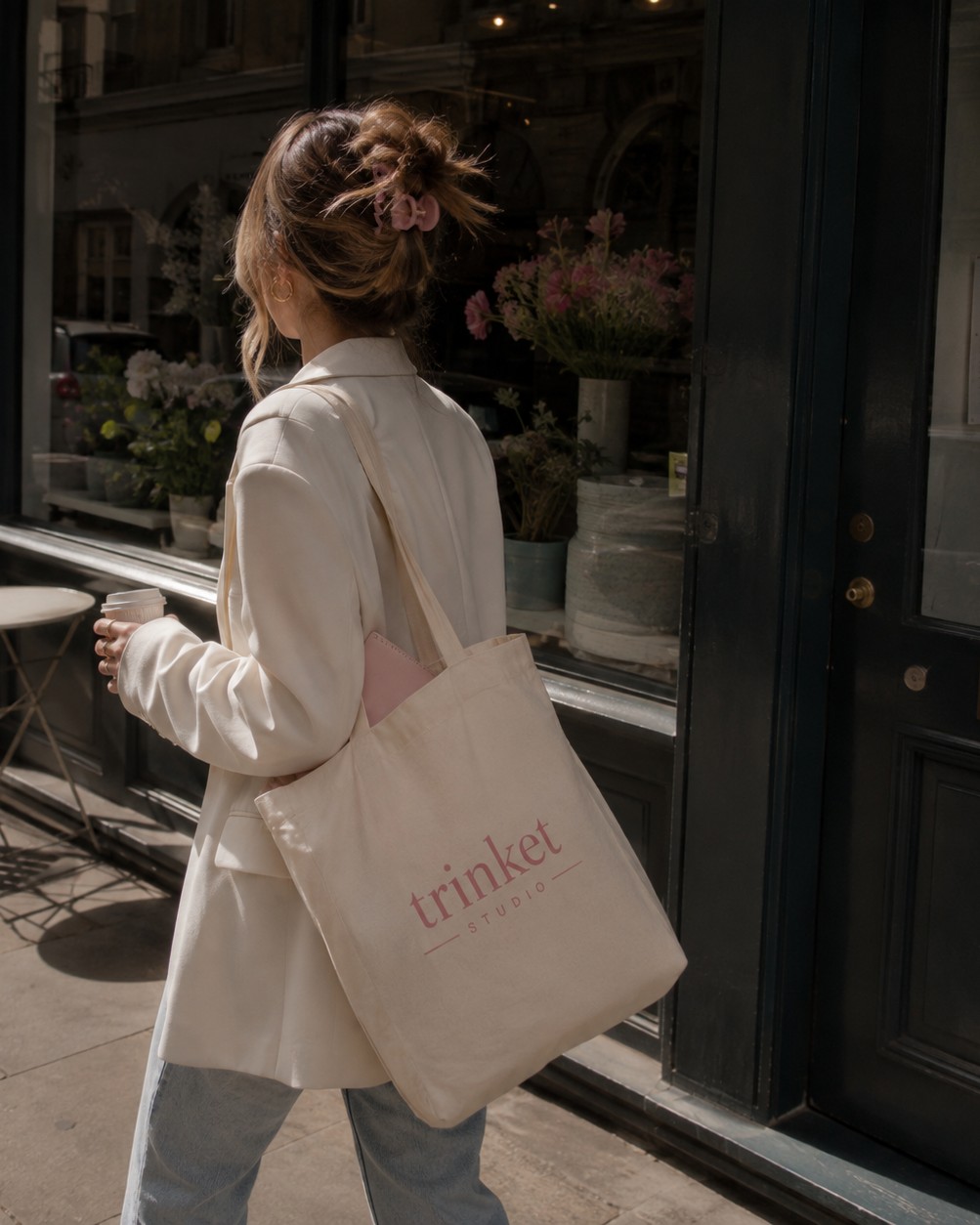 Woman walking past a city storefront carrying a Trinket Studio tote bag
